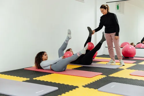 Clase de pilates suelo con pelotas; la profesora corrige a una alumna